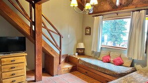 A room with a wooden staircase, a bed with patterned bedding, a TV on a wooden dresser, and a window with curtains.