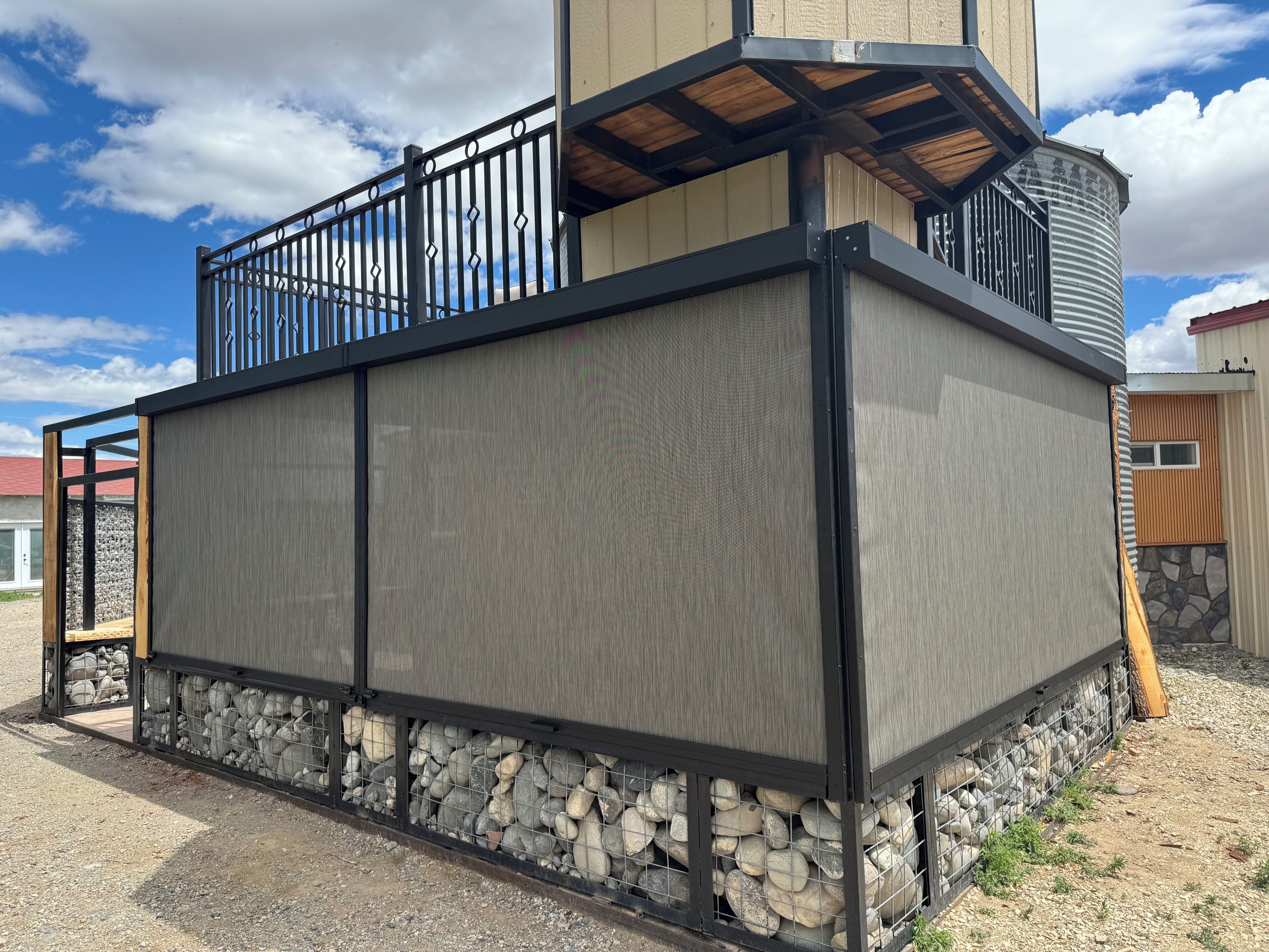 A building with a stone foundation, a metal fence, and a wooden deck.