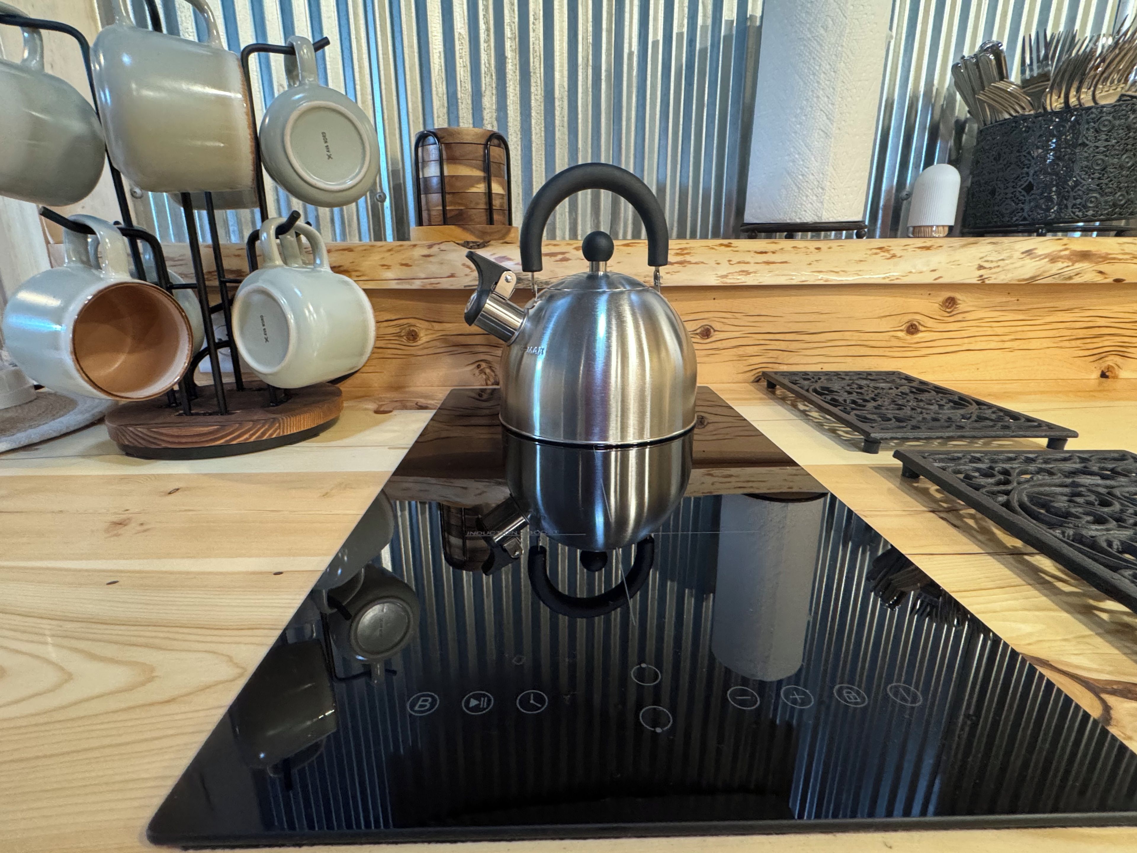 Une cuisine avec une bouilloire en acier inoxydable posée sur une plaque de cuisson à induction noire, un plan de travail en bois et un mur à rayures en arrière-plan.