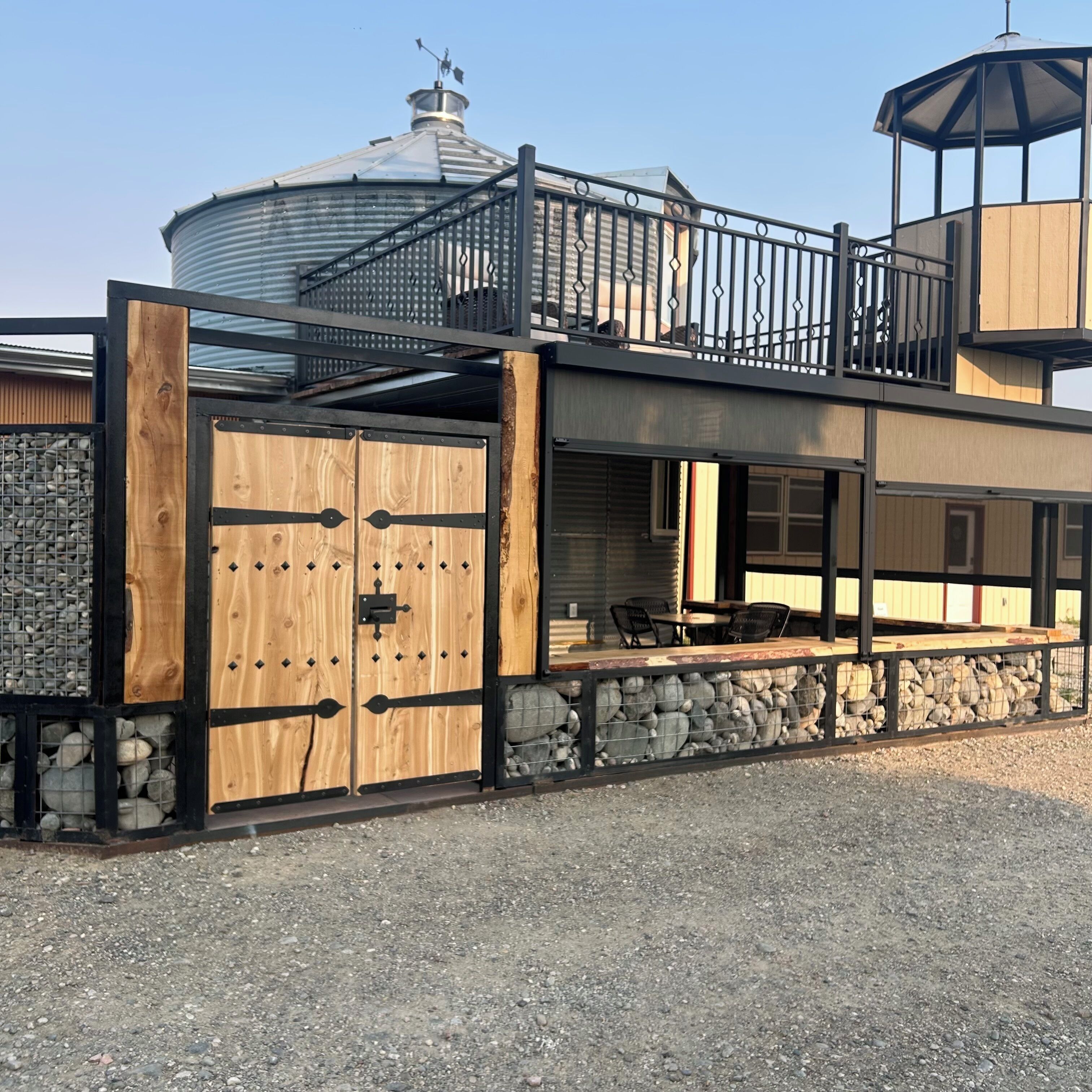 A modern building with a covered outdoor seating area, a large water tank, and a balcony with a metal railing.