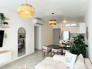 A modern living room with a sofa, dining table, and hanging lights. - Stylish 2BR Condo with Pool, BBQ and Tropical Views in Punta Cana (Punta Cana)