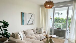Ein modernes Wohnzimmer mit einem Ecksofa, einem kleinen runden Tisch und einem großen Fenster mit Blick auf Grünflächen.