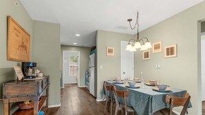 Een eetruimte met een tafel voor vier personen, houten stoelen, een kroonluchter en een keuken op de achtergrond.