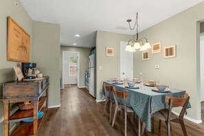 A dining area with a table set for four, wooden chairs, a chandelier, and a kitchen in the background. - The Vista Condo Great Views (Branson)