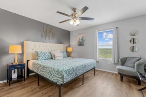 A bedroom with a bed, two bedside tables with lamps, a ceiling fan, a window with curtains, and a chair. - The Vista Condo Great Views (Branson)