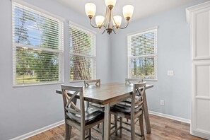 A dining area with a wooden table and chairs, large windows with blinds, and a chandelier. - The Cloisters at Myrtlewood  4 Bedroom Golf & Family Retreat, (Myrtle Beach)