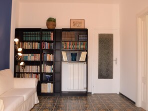 Ein Zimmer mit einem weißen Sofa, einem Bücherregal, einer Heizung und einer Tür mit strukturierter Wand.