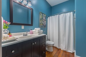 A bathroom with a blue wall, a white sink, a dark cabinet, a white toilet, and a shower curtain. - Junction On James!  Historical home with the comfort of modern amenities. (Dayton)