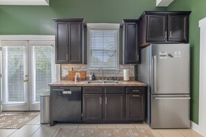 A kitchen with dark cabinets, a stainless steel refrigerator, a dishwasher, and a window with blinds. - Junction On James!  Historical home with the comfort of modern amenities. (Dayton)