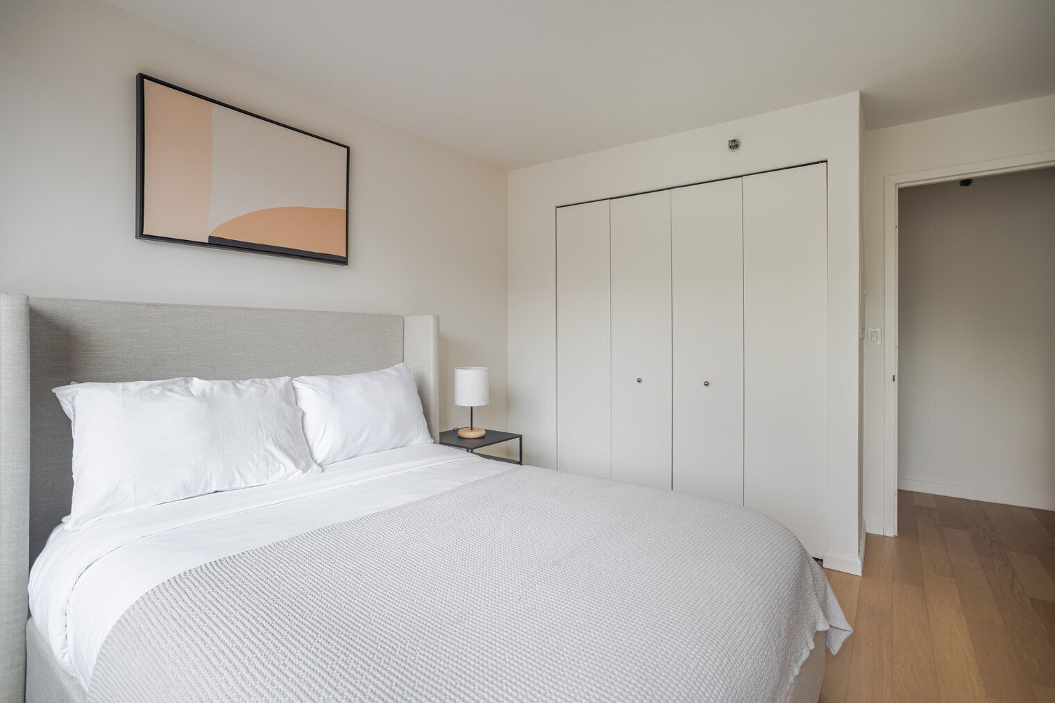 Quarto com cama, mesa de cabeceira, luminária, guarda-roupa e porta.