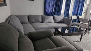 Un salon moderne avec un canapé d’angle, une table basse en verre et un coin repas avec des chaises.