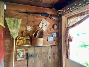 Ein rustikales Blockhaus-Interieur mit Holzboden, Besen, Schaufel, Holzschaufel, einer Zeitschrift, einer Uhr und einem Fenster mit Vorhängen.