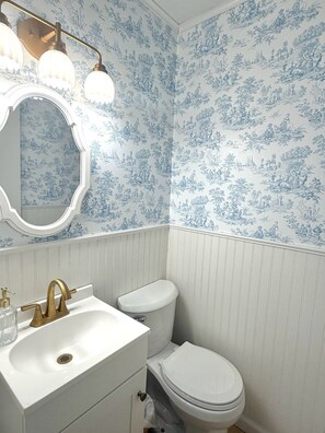 A bathroom with a toilet, sink, and vanity, featuring blue floral wallpaper and white paneling.