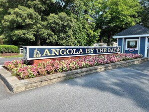 Une enseigne indiquant « Angola by the Bay », avec un petit bâtiment et un parterre de fleurs devant.