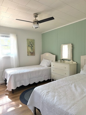 A bedroom with two single beds, a ceiling fan, a dresser, a mirror, and a painting on the wall.