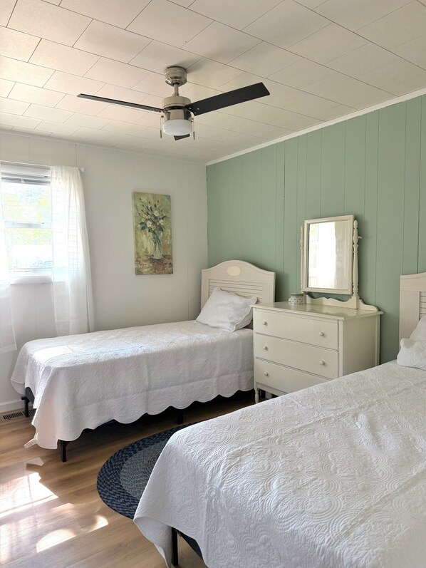 Un dormitorio con dos camas individuales, un ventilador de techo, un aparador, un espejo y un cuadro en la pared.