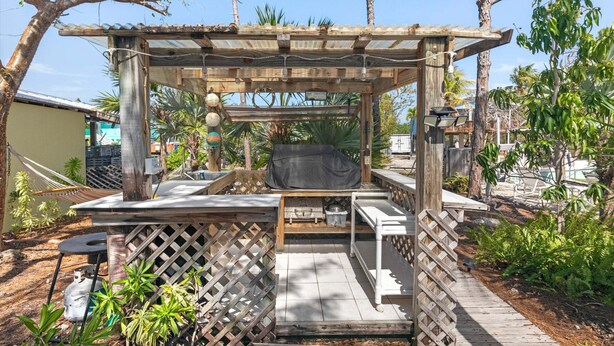 Een houten pergola met een barbecuegedeelte, omringd door een houten terras en een lattenhek.