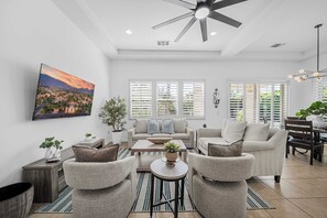 Un salon moderne doté d’un ventilateur de plafond, d’un grand téléviseur et d’un coin repas avec une table et des chaises.