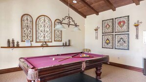 Een pooltafel met een rode viltkleed, een kroonluchter en decoratieve muurkunst.