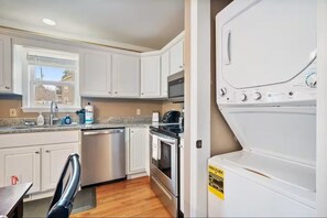 A kitchen with white cabinets, a stainless steel dishwasher, an oven, and a white washing machine. - Serene 2-bedroom cottage with fireplace in charming Gatlinburg (Gatlinburg)