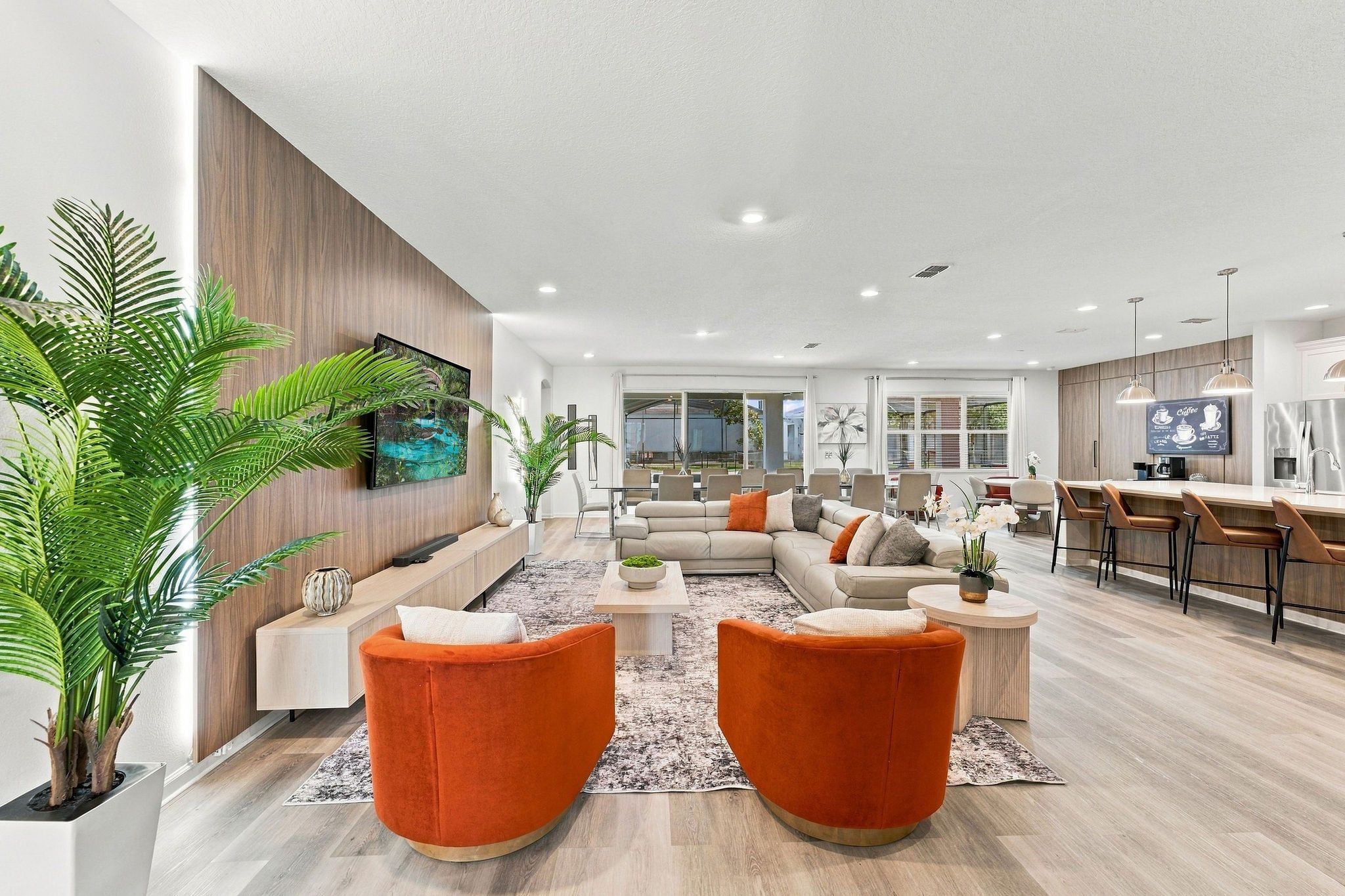 A modern living room with a sofa, orange chairs, a coffee table, and a TV mounted on the wall.