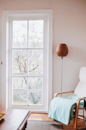 Ein Zimmer mit großem Fenster, einer Stehlampe, einem Sessel und einem Tisch.
