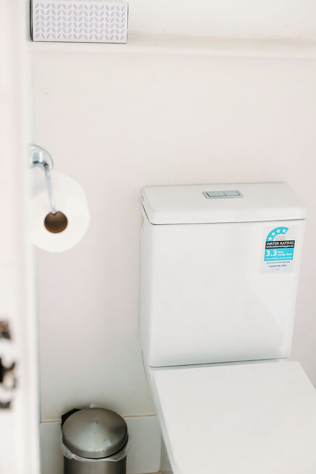 A white toilet with a water rating sticker, a toilet paper holder, and a trash bin.