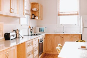 Eine moderne Küche mit Holzausstattung, einer eingebauten Mikrowelle, einem Toaster und einem Fenster mit Jalousien.