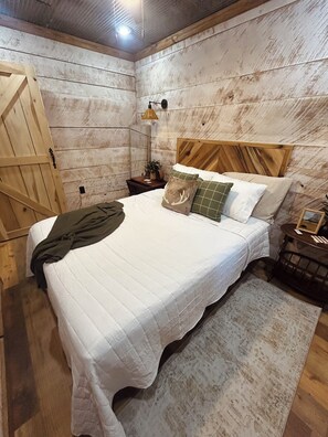 Une chambre à coucher avec une tête de lit en bois, un lit recouvert de linge de lit blanc, une table de chevet avec une lampe et un plancher en bois rustique.