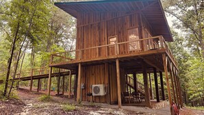 A wooden cabin with a balcony, a staircase, and an air conditioning unit. - Treehouse+Quiet Escape+National Forest+Firepit (Falkner)