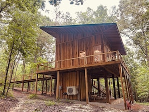 A wooden cabin with a balcony, a staircase, and an air conditioning unit.
