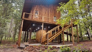 A wooden cabin with a balcony and a staircase, surrounded by trees. - Treehouse+Quiet Escape+National Forest+Firepit (Falkner)