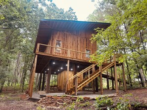 A wooden cabin with a balcony and a staircase, surrounded by trees.