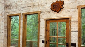 A rustic interior with wooden walls, large windows, and a door with a glass panel. - Treehouse+Quiet Escape+National Forest+Firepit (Falkner)