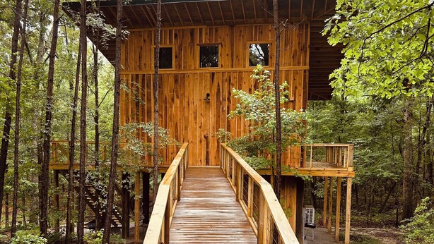 A wooden cabin with a wooden deck leading to a door, surrounded by a forest. - Treehouse+Quiet Escape+National Forest+Firepit (Falkner)