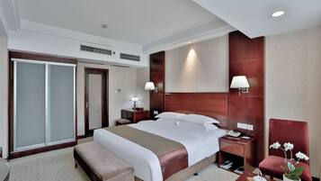 Ein Hotelzimmer mit einem großen Bett, einem Schreibtisch, einem Stuhl, einem Kleiderschrank und einem Blumentopf.
