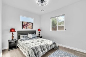 A bedroom with a bed, two bedside tables, a ceiling fan, a window, and a painting on the wall. - Sonoran Summer Stay | Near Downtown & UofA (Tucson)