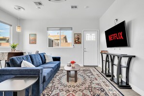 A modern living room with a sofa, a coffee table, a TV mounted on the wall, and a patterned rug. - Sonoran Summer Stay | Near Downtown & UofA (Tucson)