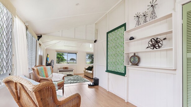 A spacious room with a large window, wicker furniture, a green decorative panel, and a clock on the wall. - Ocean Soul Unit 1 (Burnett Heads)