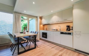 Eine moderne Küche mit Essbereich, ausgestattet mit Backofen, Geschirrspüler und Kaffeemaschine.