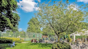 Ein Park mit einem großen Baum, Sitzgelegenheiten im Freien und einem eingezäunten Bereich.