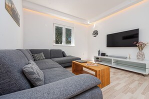 A modern living room with a grey sectional sofa, a wooden coffee table, a flat-screen TV, and a minimalist white entertainment unit. - Olive House Pool & Garden, Zemunik Donji, Croatia (Zemunik Donji)