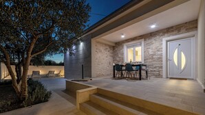 Une terrasse extérieure moderne, avec des murs en pierre, un espace repas avec des chaises et un escalier menant à une porte.