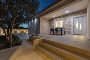 A modern outdoor patio with stone walls, a dining area with chairs, and a staircase leading to a door. - Olive House Pool & Garden, Zemunik Donji, Croatia (Zemunik Donji)