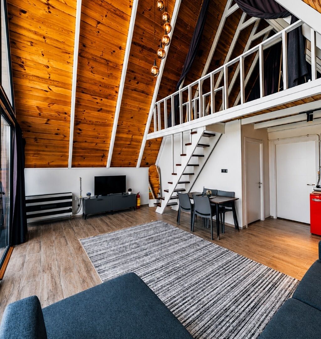 Et loftrum med træloft, trappe, spiseplads og fjernsyn.