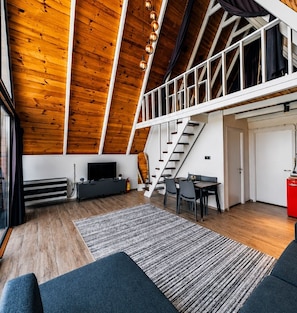 A loft-style room with a wooden ceiling, a staircase, a dining area, and a television.