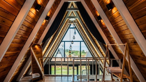 A triangular attic bedroom with a large window, a bathtub, and a bed.
