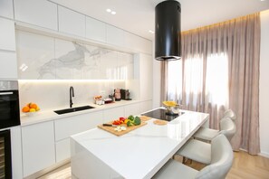 A modern kitchen with a central island, white cabinetry, a black range hood, and a window with curtains.