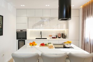A modern kitchen with white cabinetry, a central island with seating, a built-in oven, and a black range hood.