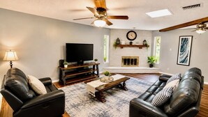 A living room with a fireplace, leather sofas, a TV, and a ceiling fan.